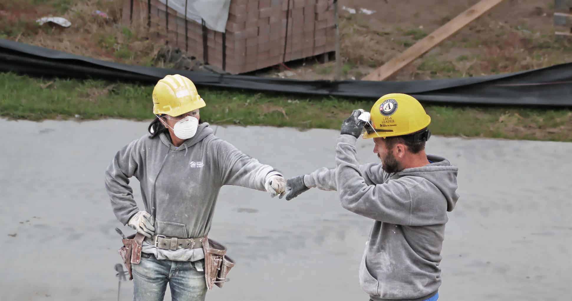 Two people in hard hats fist-bumping