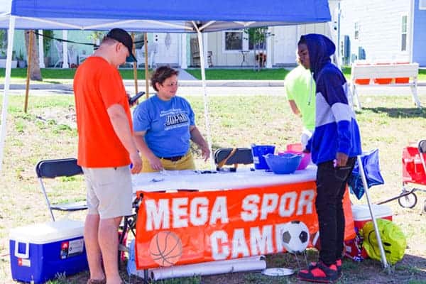 Young man speaking to women behind Mega Sports Camp table
