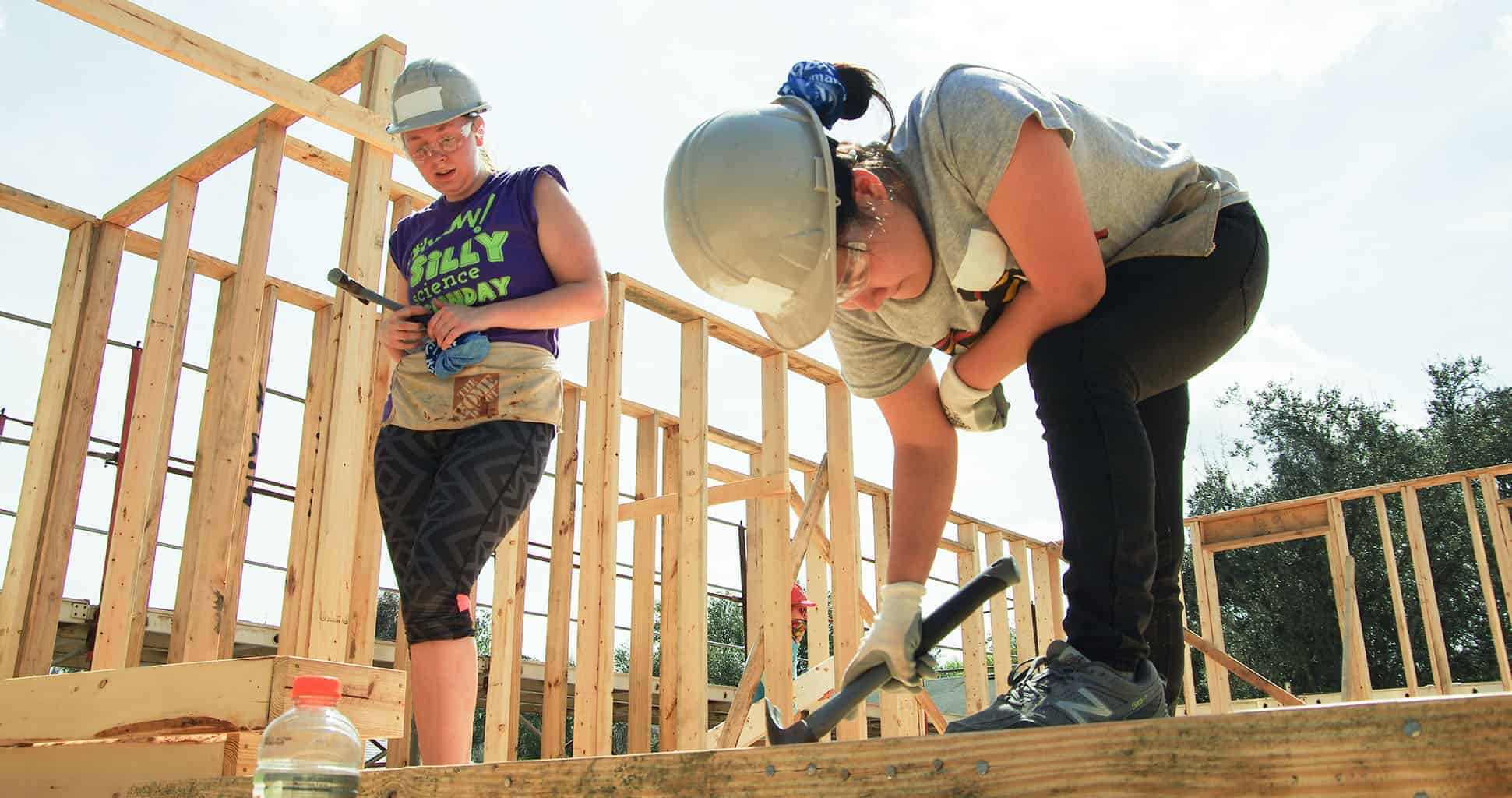 Two women in hard hats build walls