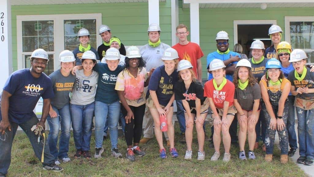 Group of students wearing hard hats in front of home