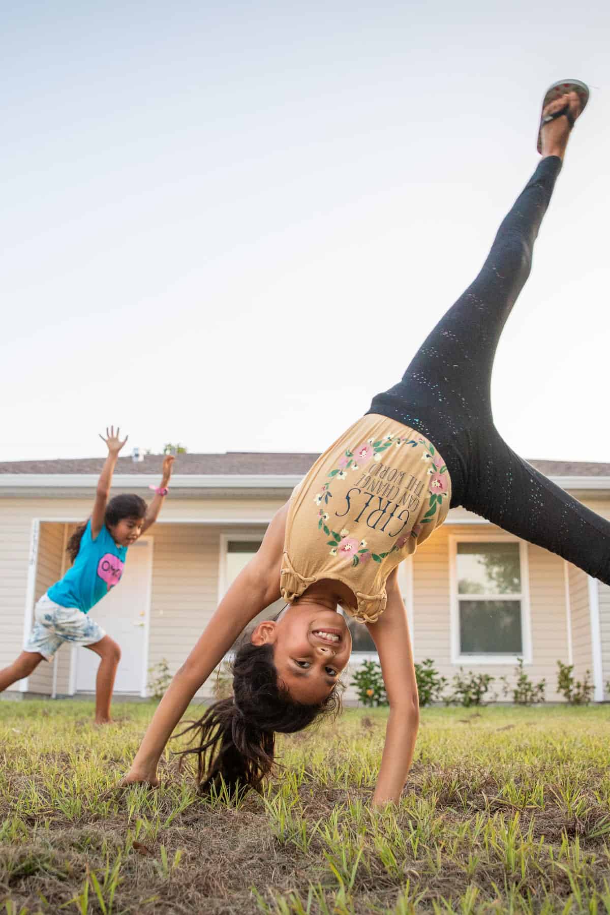 Cartwheels Jamielynn (beige shirt, 8) and Joselynn (blue shirt, 7) play in the front yard of their new house.