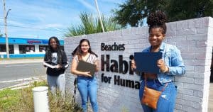 3 young women holding laptops in front of Beaches Habitat sign
