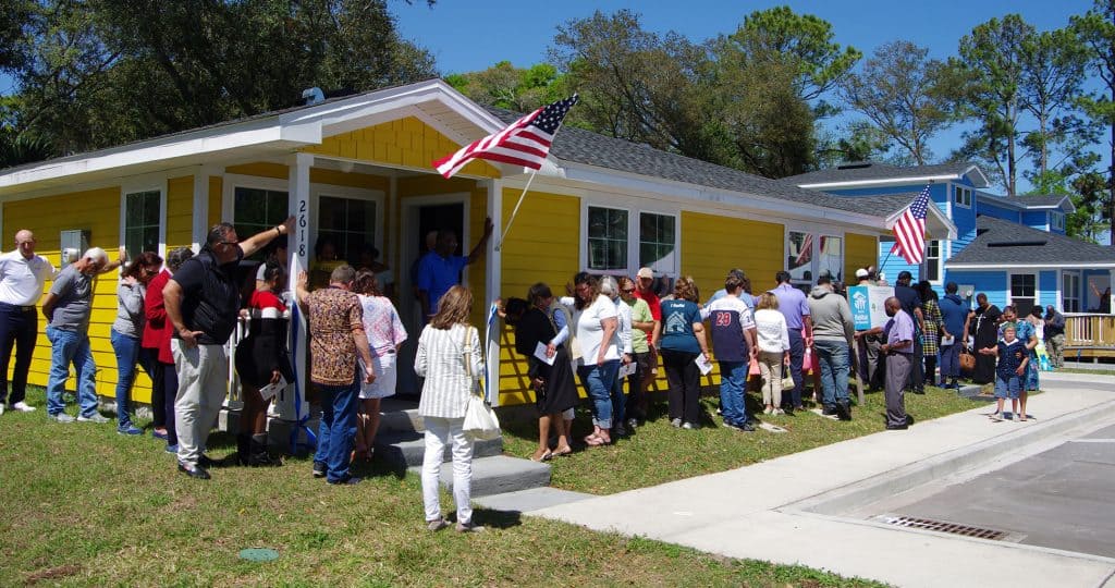 A group of people gather around a yellow duplex
