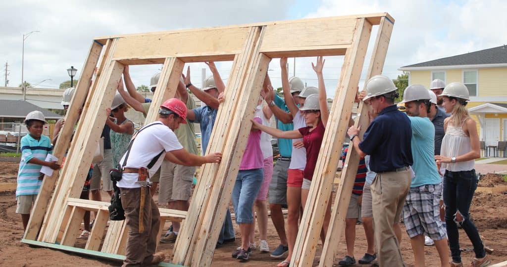 Group of people lifting wood frame of wall