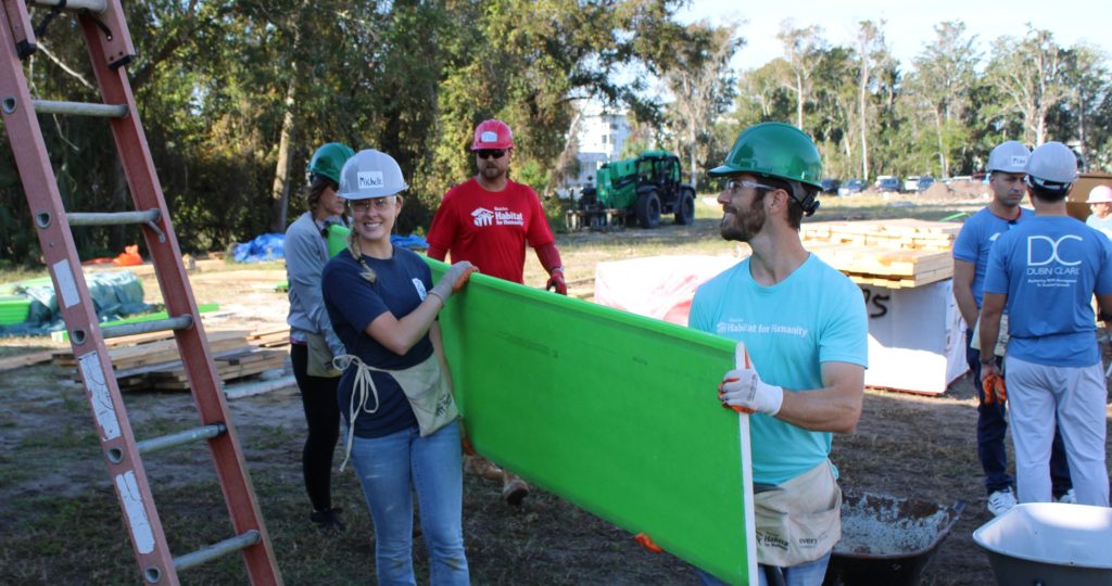 Volunteers carrying a green panel at a Habitat build site.