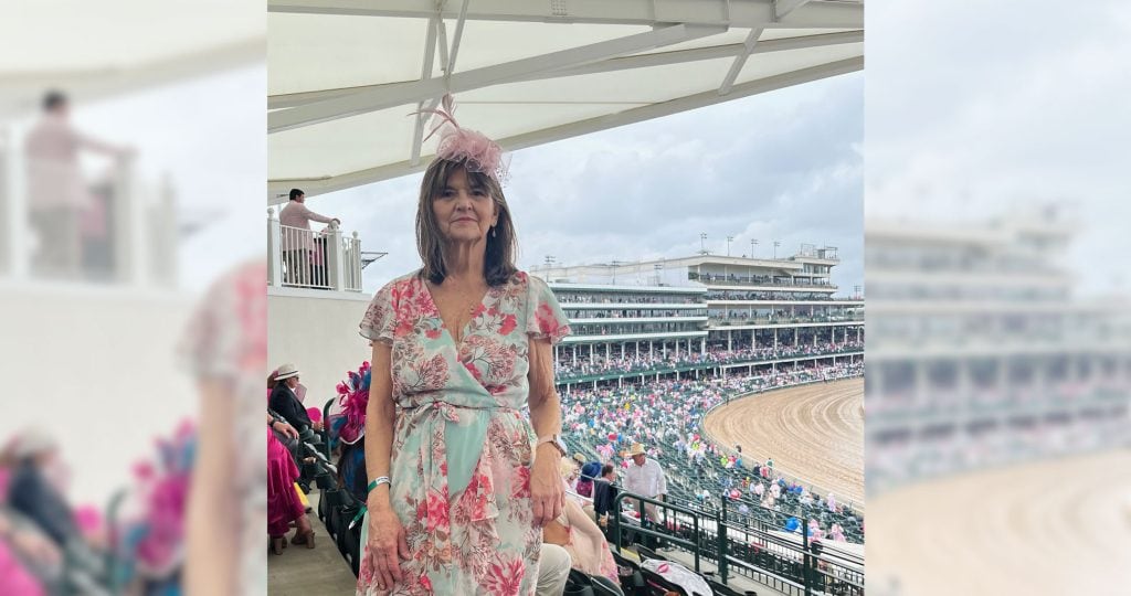 Debbie smiling at the Kentucky Derby, wearing a floral dress and sun hat.